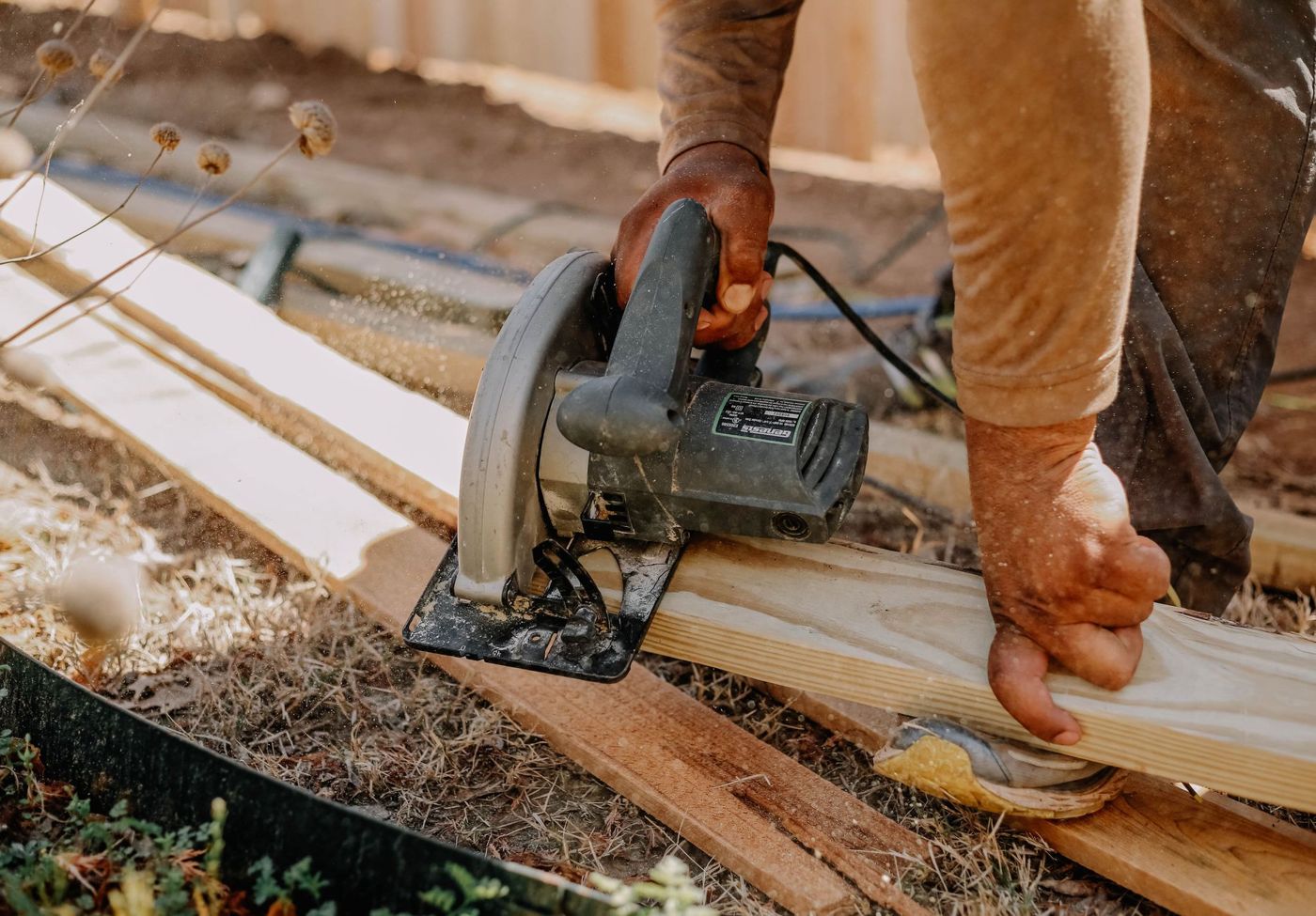 Close-up of a carpenter cutting a lumber board with a circular saw outdoors, sawdust in the air