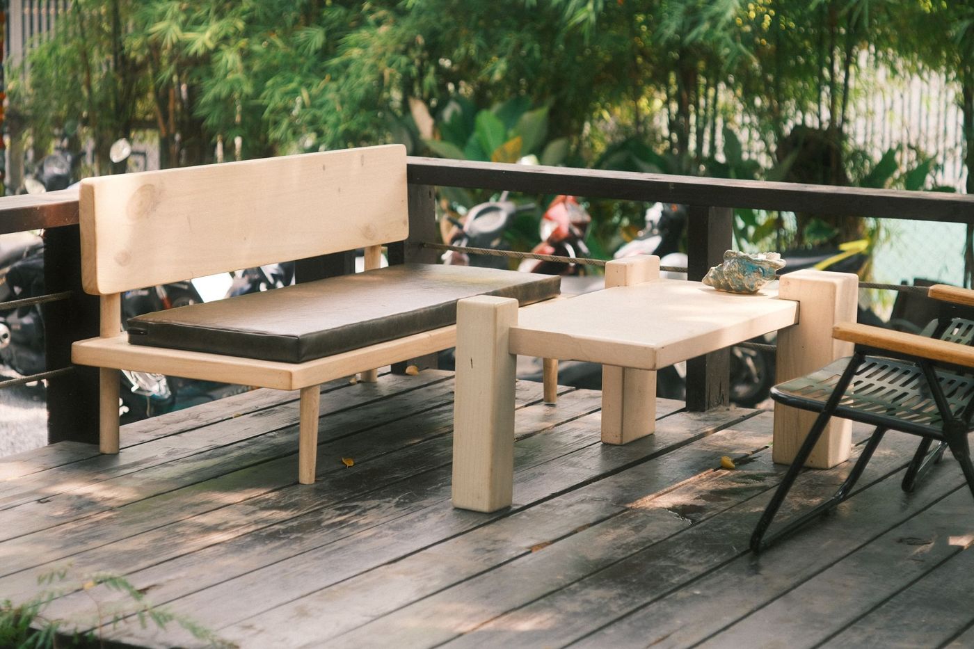 Light wood bench and low table on a dark plank deck with a dark wood railing and horizontal cable infill