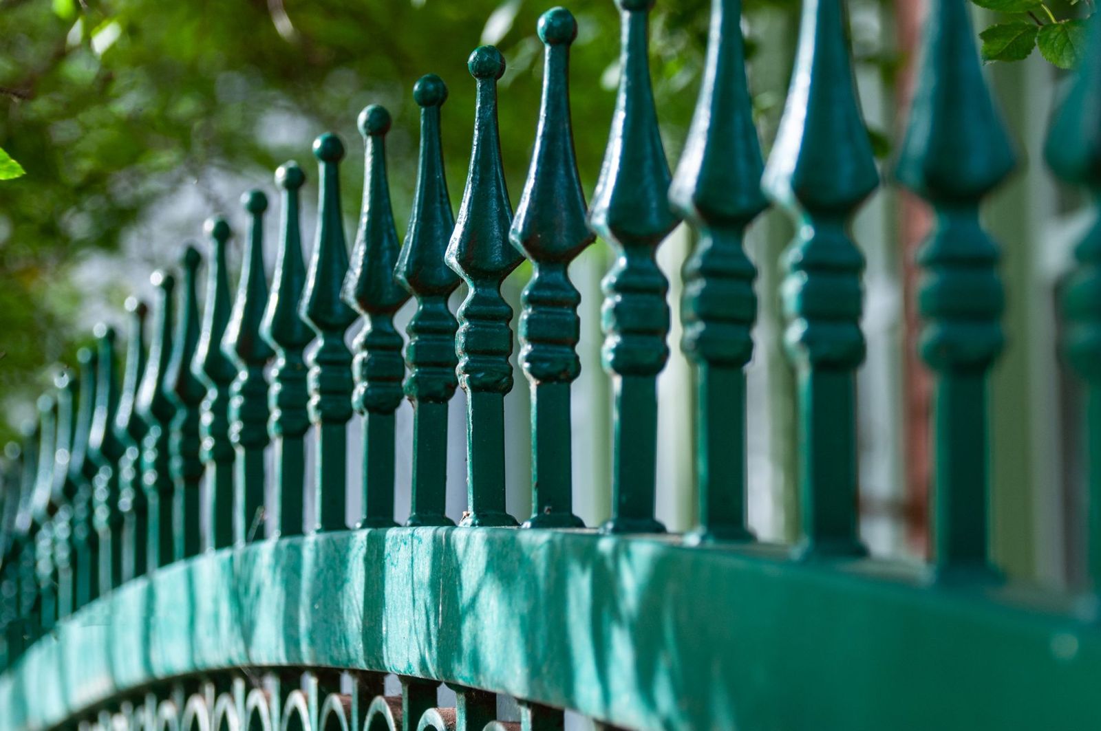 Close-up of a green-painted ornamental metal fence with rows of decorative spear-tipped pickets