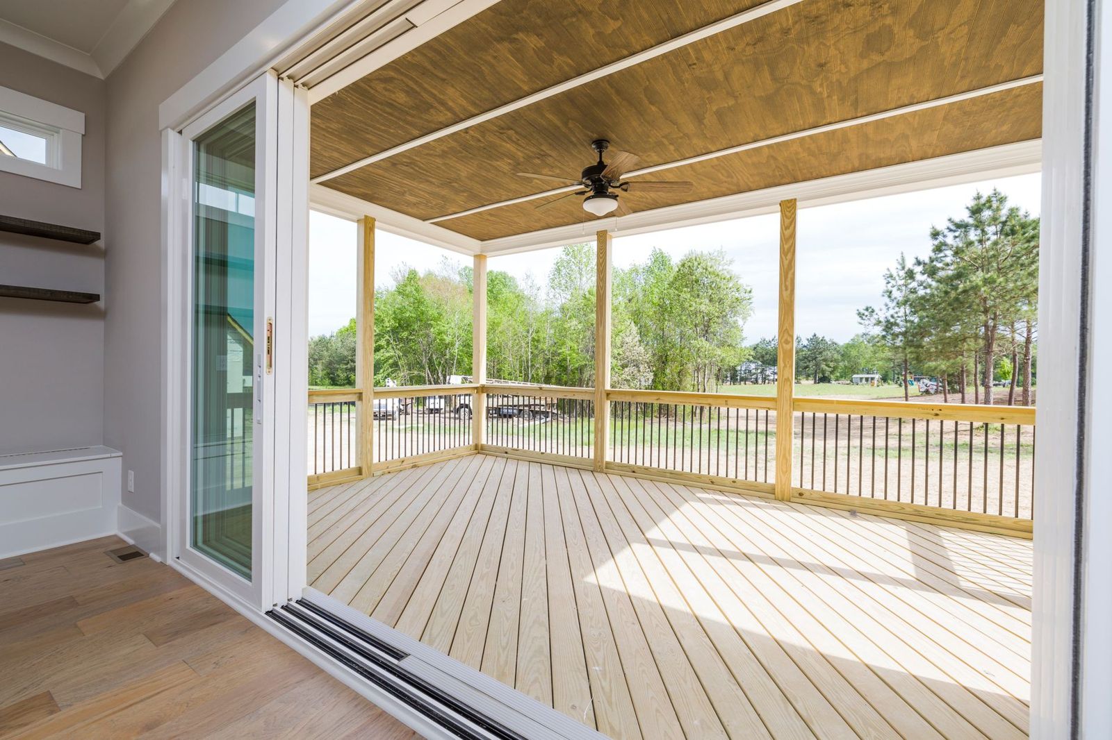 Covered porch deck of new pale pressure-treated boards and railings with a wood ceiling and fan, seen through open sliding doors
