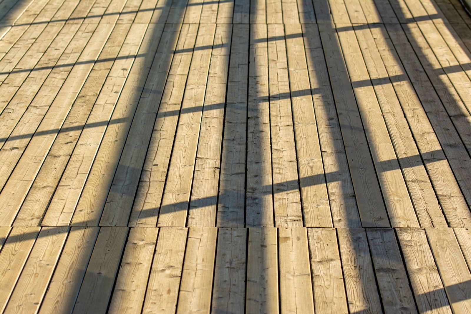 Close-up of pale wood deck boards in low sunlight with long railing shadows falling across them